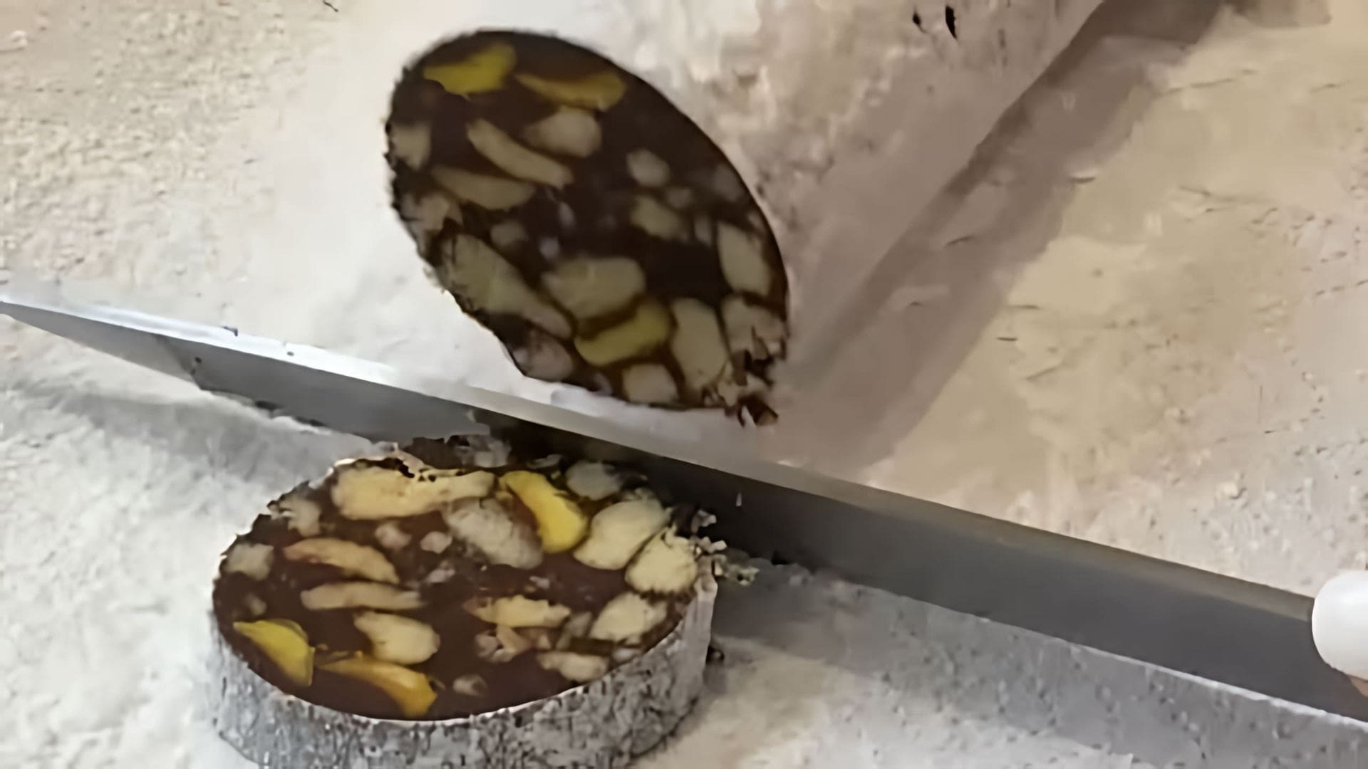 В этом видео демонстрируется процесс приготовления шоколадной колбасы из печенья и орехов